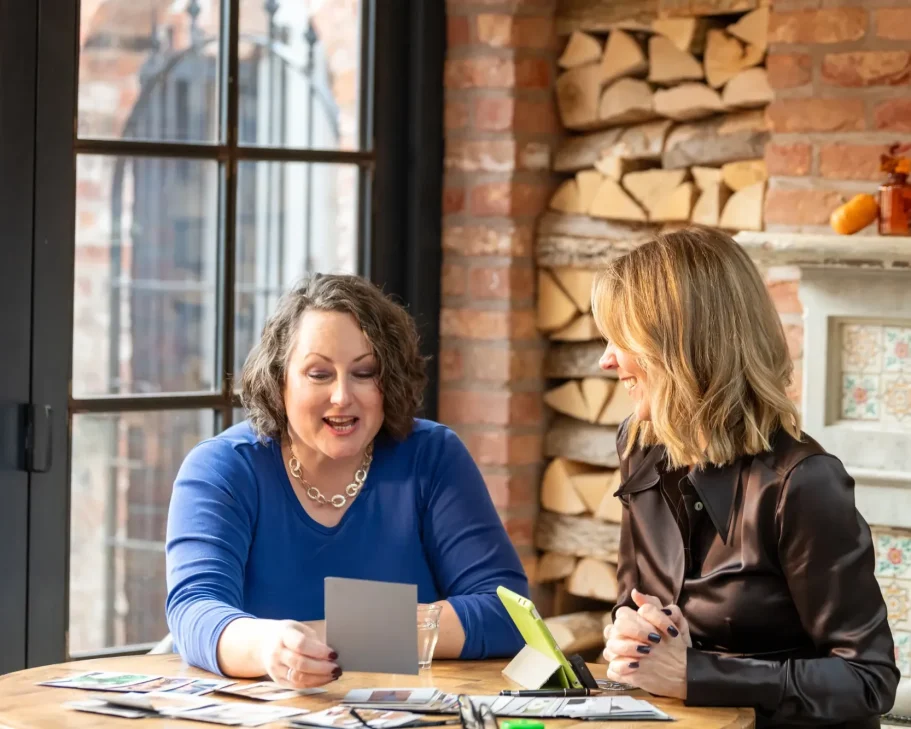 Two women are discussing photographs at a table in a cozy setting.